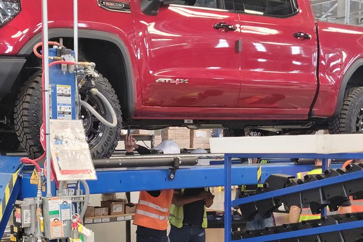 Technicians installing a bedliner into a truck bed on a production lift