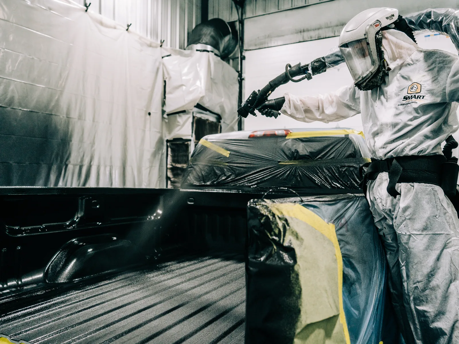 Technician spray-applying a LINE-X protective coating inside a truck bed