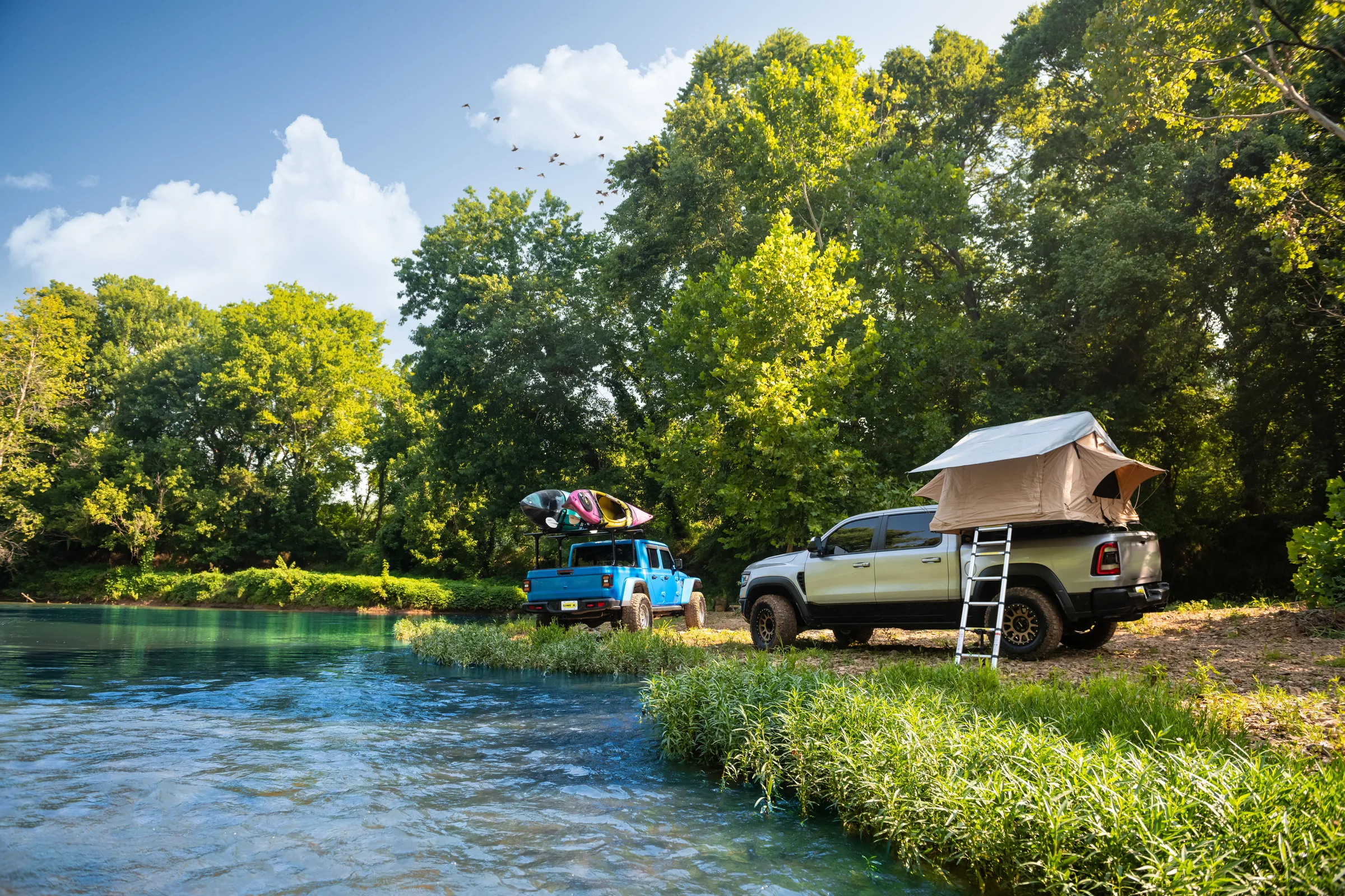 Two LINE-X-equipped trucks parked beside a river during an off-road outing
